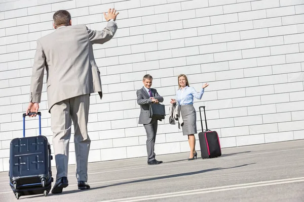 Businessman carrying luggage waving to colleagues — Stock Photo, Image