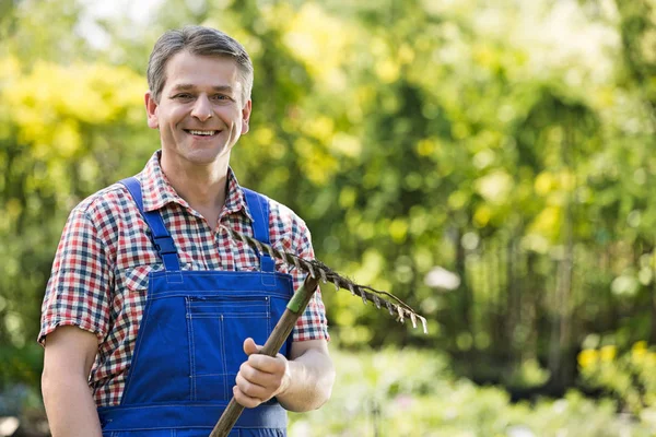 Jardinero sonriente sosteniendo rastrillo — Foto de Stock