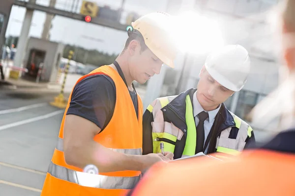 Male workers discussing over clipboard — Stock Photo, Image