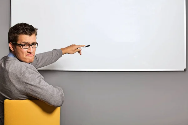 Businessman pointing at whiteboard and making face — Stock Photo, Image