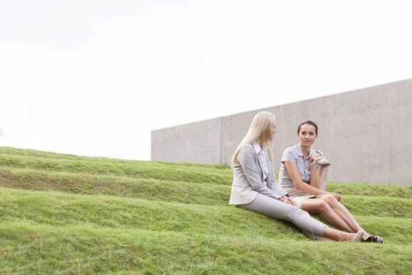 Vrouwelijke ondernemers zittend op gras stappen — Stockfoto