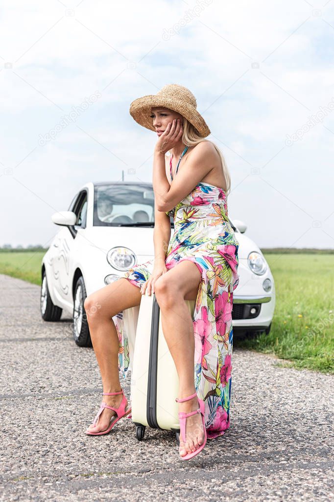 woman sitting on luggage by car