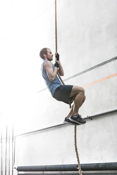 Man climbing rope in crossfit gym — Stock Photo, Image