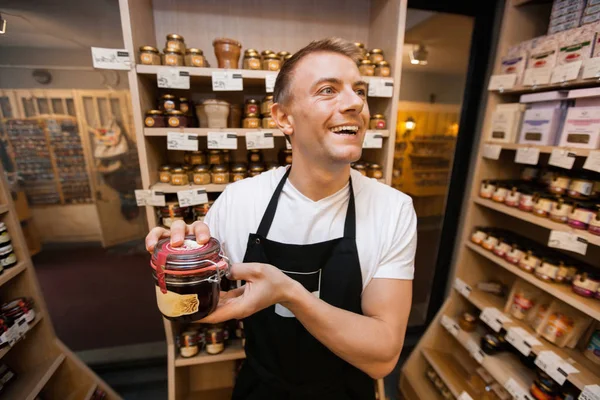 Cheerful salesman holding jar of jam — Stock Photo, Image
