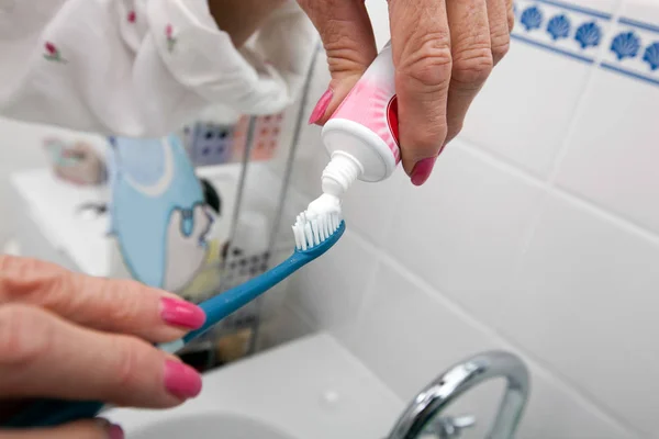 Женщина накладывает зубную пасту на щетку — стоковое фото
