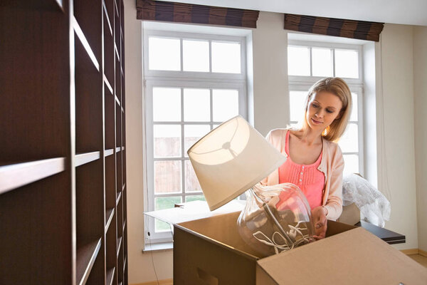 Женщина вытаскивает лампу из картонной коробки
