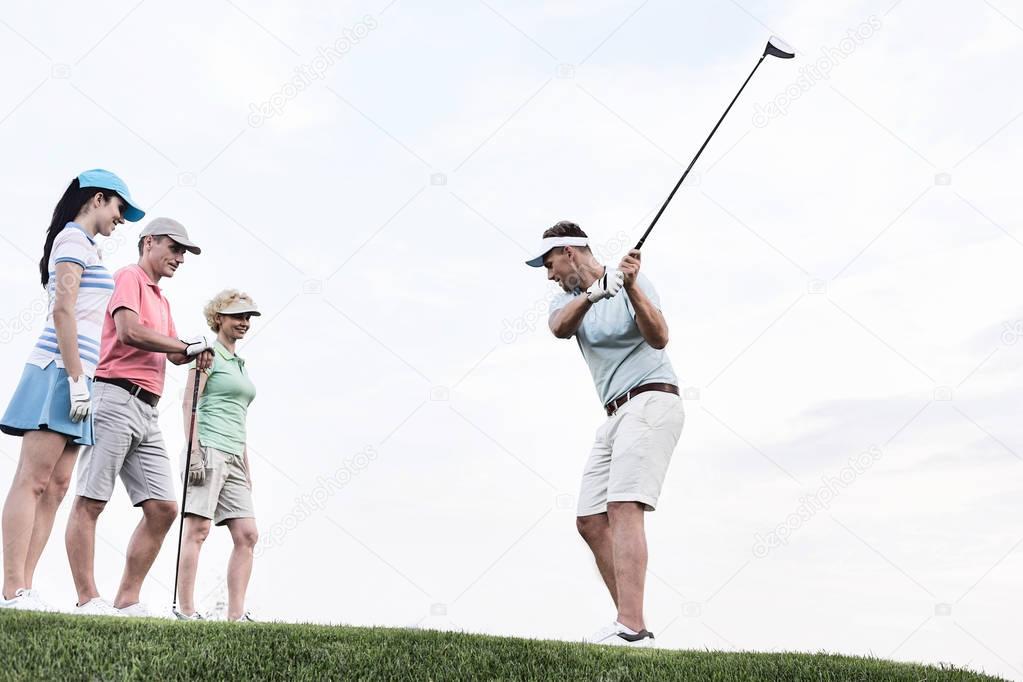 Friends looking at man playing golf 