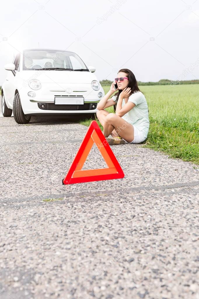 woman sitting by broken down car