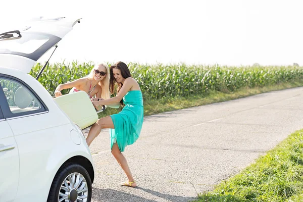 Friends pushing luggage in car trunk — Stock Photo, Image