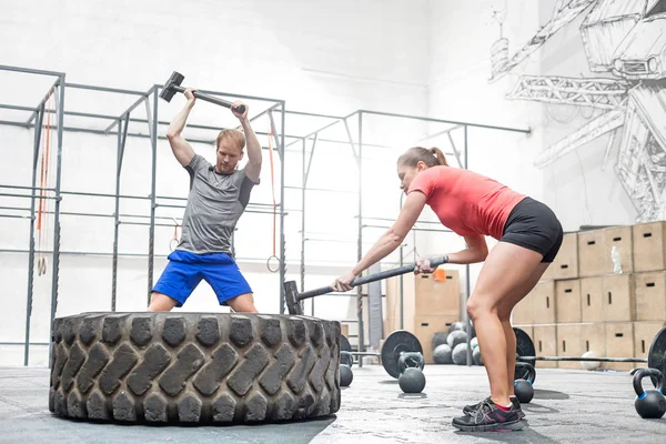Man and woman hitting tire with sledgehammer — Stock Photo, Image