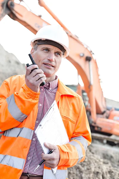 Supervisor holding clipboard while using walkie-talkie — Stock Photo, Image