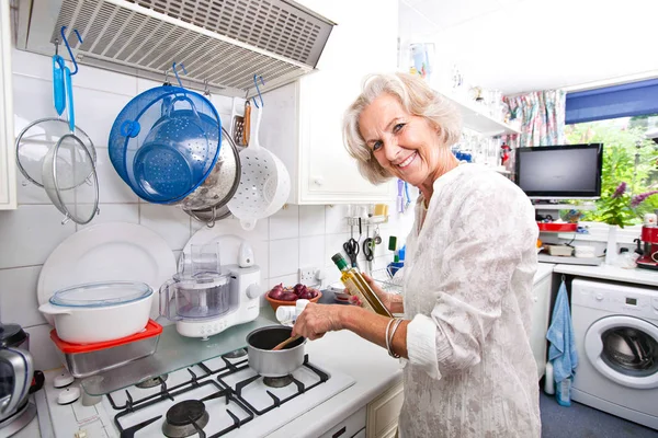 Senior woman adding olive oil — Stock Photo, Image