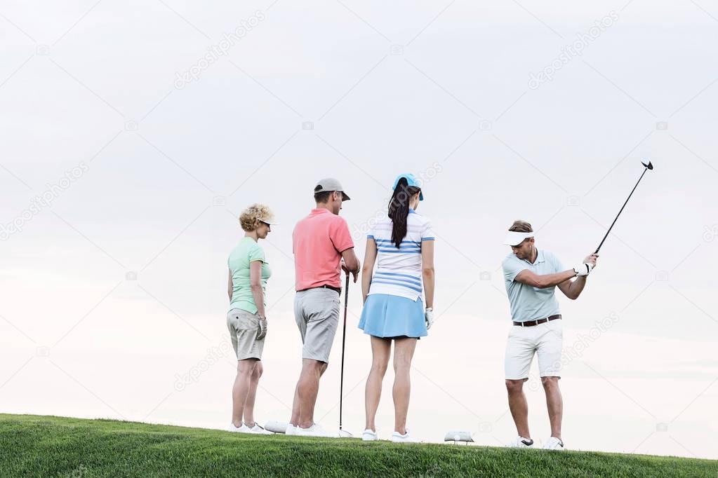 friends looking at man playing golf 