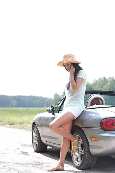 Woman with cell phone leaning on convertible — Stock Photo, Image