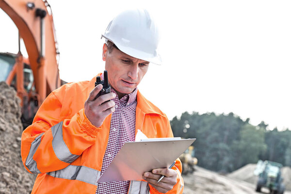 Supervisor reading clipboard while using walkie-talkie