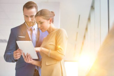 Ofisteki işadamına dijital tableti gösteren iş kadını. Arka planda sarı lens ışığı var.