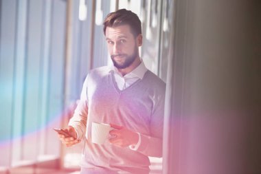 Ofis salonunda sarı ışıklı akıllı telefon kullanan bir işadamı.