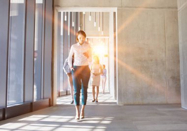Ofisteki sarı ışıklı akıllı telefonu kullanarak yürüyen bir iş kadını.