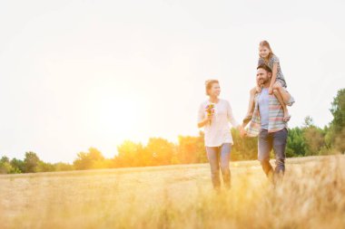 Mutlu aile çiftlikte gökyüzüne karşı, baba kızını omuzlarında tutuyor.