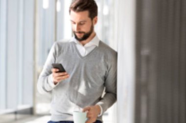 Genç çekici iş adamı ofis salonunda sarı ışıklı akıllı telefon kullanıyor.