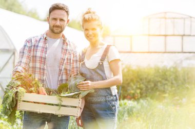 Happy couple holding vegetable crate at farm