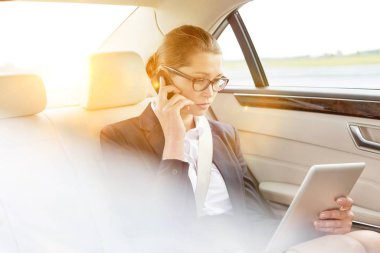 Genç çekici bir iş kadını, arka planda sarı bir mercekle arabada otururken akıllı telefondan konuşuyor. 