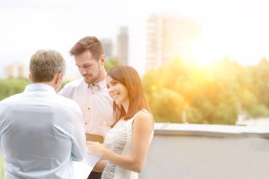 İş adamları ofis çatısında arka planda sarı lens fişeğiyle ilgili planları tartışıyor. 