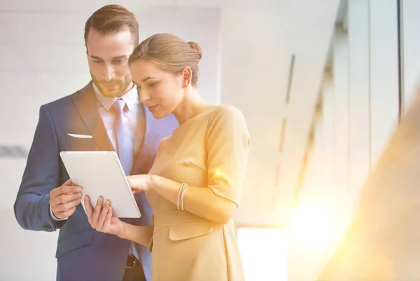 黄色のレンズフレアを背景にオフィスホールでビジネスマンにデジタルタブレットを示すビジネスマン女性 — ストック写真