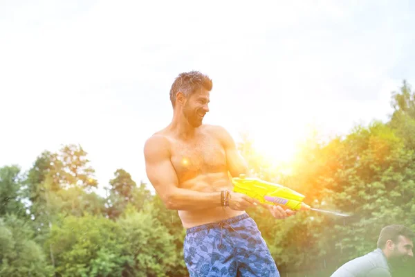 Foto Van Man Spelen Sproeien Waterpistool Aan Zijn Vrienden Terwijl — Stockfoto