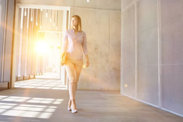 黄色のレンズフレアを背景にオフィスホールを歩くビジネスマンの女性 — ストック写真
