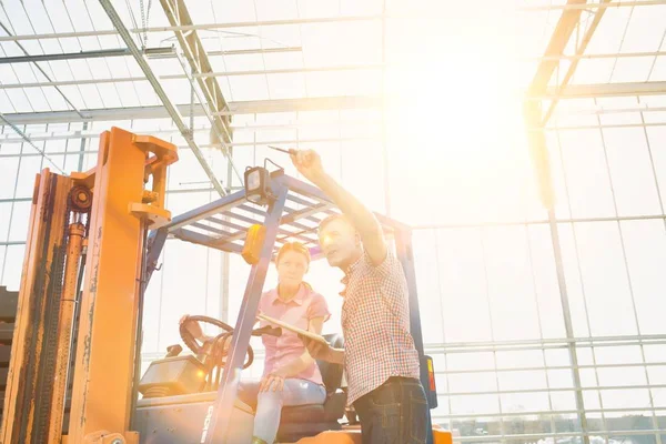 Farmer discussing with coworker on forklift over crates at storehouse