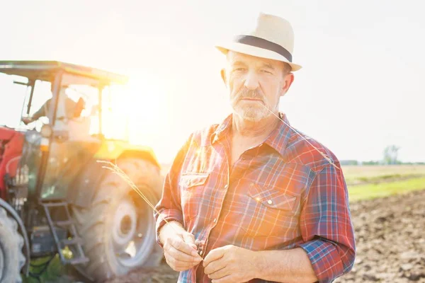 Portrait of confident senior farmer standing against tractor at farm