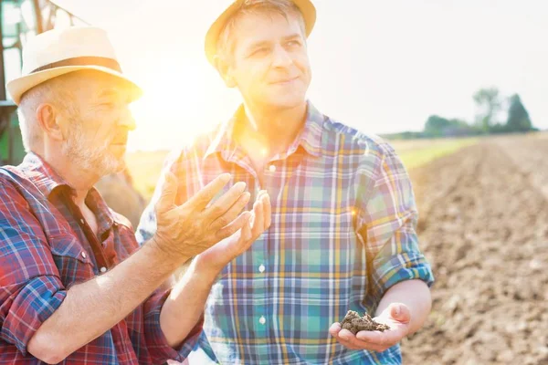 Farmers discussing over soil in field with yellow lens flare in background