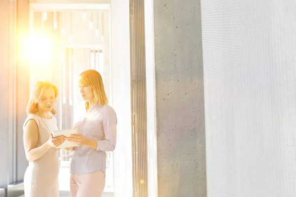 黄色のレンズフレアを背景にオフィスホールでデジタルタブレット上の計画を議論ビジネスマン女性 — ストック写真