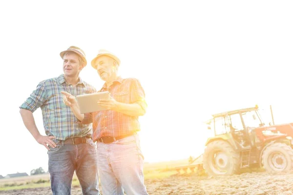 Farmers talking while using digital tablet at farm on sunny day