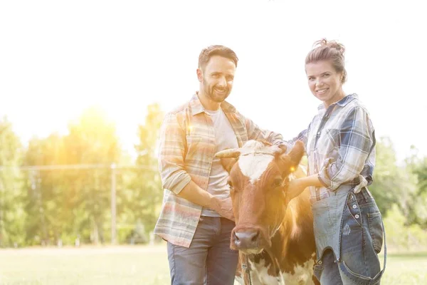 Smiling couple standing with cow at farm