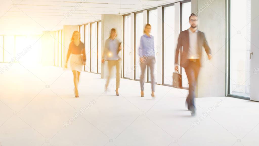 Business people walking in office hall with yellow lens flare in background