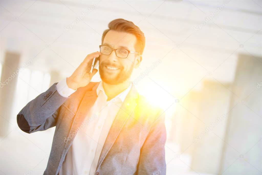Businessman talking on smartphone in new office with yellow lens flare in background