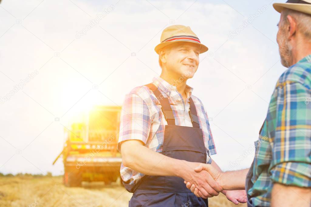 Farmers shaking hands while standing on field at farm