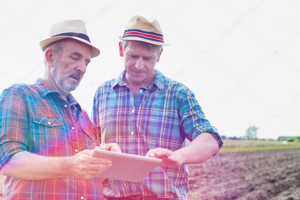 Farmers talking while using digital tablet at farm on sunny day