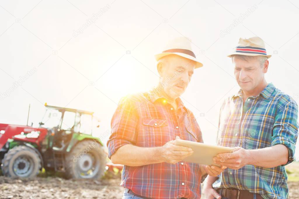 Farmers talking while using digital tablet at farm on sunny day