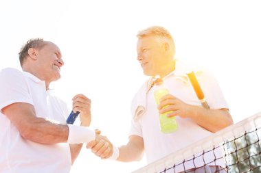 Olgun sporcular tenis kortunda el sıkışarak birbirlerini selamlıyorlar. 