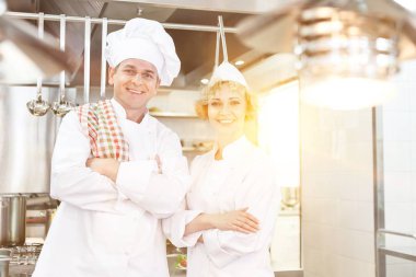 Kendine güvenen olgun aşçılar, arka planda sarı mercekle mutfak restoranında duruyorlar. 