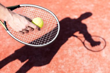 Elinde raket tutan ve arka planda sarı lens fişeği olan aktif bir adam mahkemede tenis oynuyor.