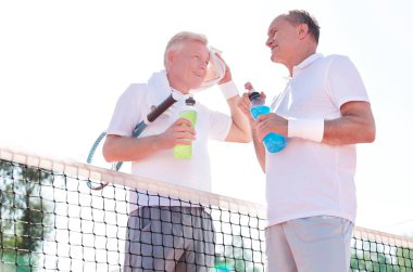 Olgun tenis atletleri mahkemede ayakta dururken enerji içeceği içiyorlar 