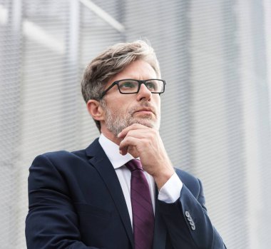 Ofisin çatısında duran düşünceli, olgun iş adamının portresi.