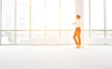 Yeni boş ofiste akıllı telefon kullanan iş kadını. Arka planda sarı lens fişeği var.