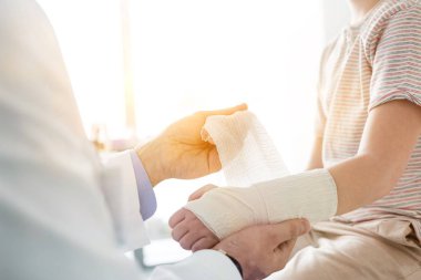 Doktor, arka planda sarı mercekli yaralı hasta bacağı bandajını ayarlıyor. 