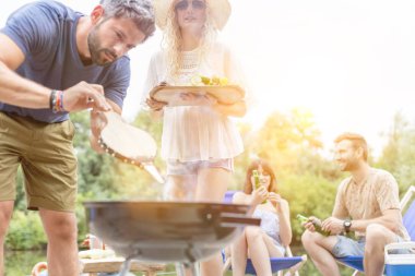 Adam kız arkadaşıyla göldeki bir piknikte ızgara yaparken Tong kullanıyor.
