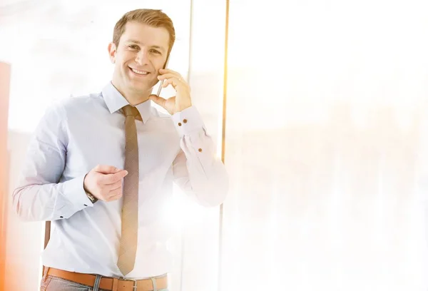 黄色いレンズフレアを背景にオフィスのスマートフォンで話している間の成熟したビジネスマンの笑顔の肖像 — ストック写真